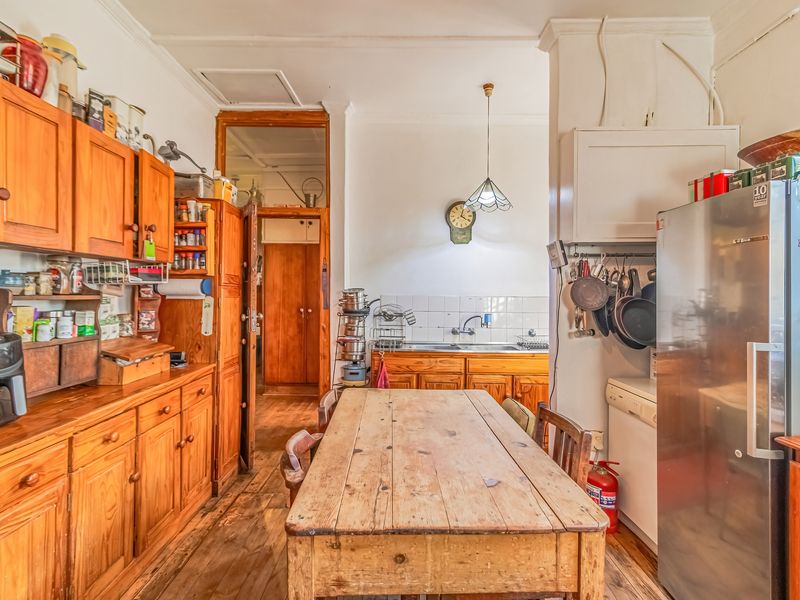 A functional kitchen featuring wooden cabinetry, tiled backsplash, and hardwood flooring, offering a traditional aesthetic with potential for modern updates.