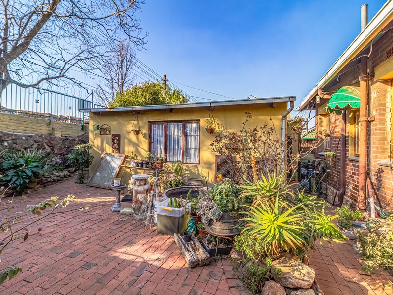 A rear courtyard featuring brick paving, a retaining wall, and a secondary structure with an awning, offering potential for outdoor living space enhancement.
