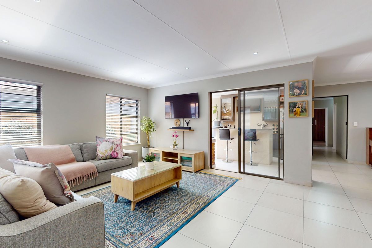 Spacious living room featuring neutral tiled flooring, recessed downlights, and sliding glass doors leading to an adjacent bar or entertainment area.