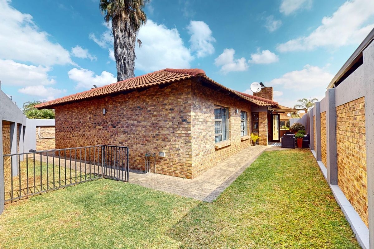 Rear view of the property featuring a face brick exterior, tiled roof, paved walkway, and a private garden area enclosed by boundary walls.