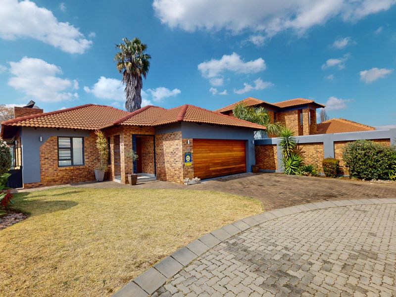 Front exterior view of a brick house featuring a tiled roof, wooden garage door, and a paved driveway with landscaped garden.