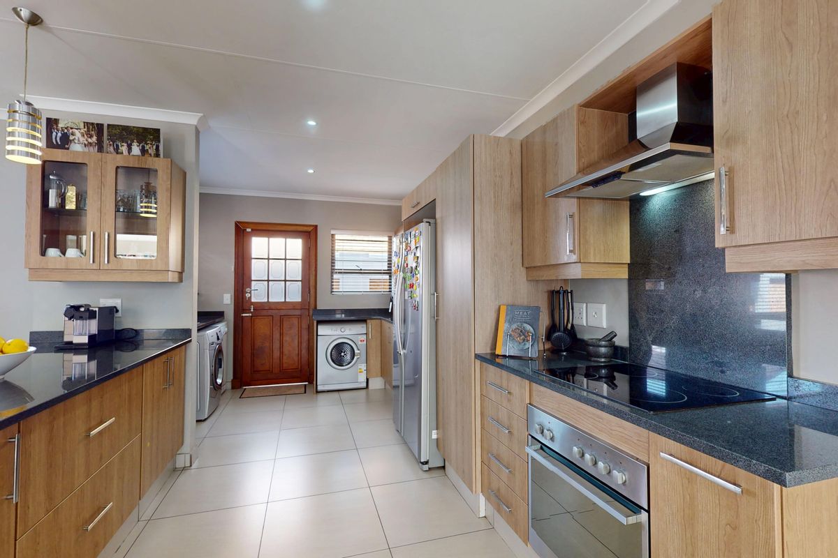 Modern kitchen featuring light wood cabinetry, dark granite countertops, integrated appliances, and tiled flooring with direct access to the exterior.