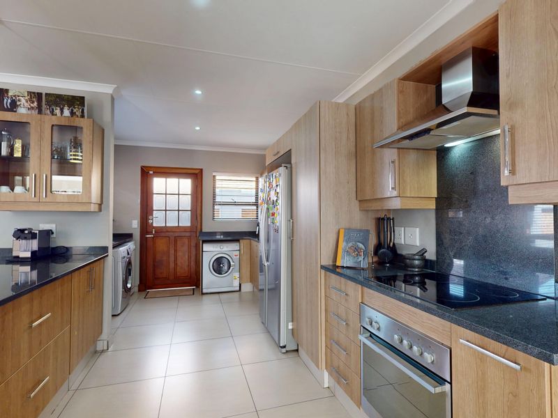 Modern kitchen featuring light wood cabinetry, dark granite countertops, integrated appliances, and tiled flooring with direct access to the exterior.
