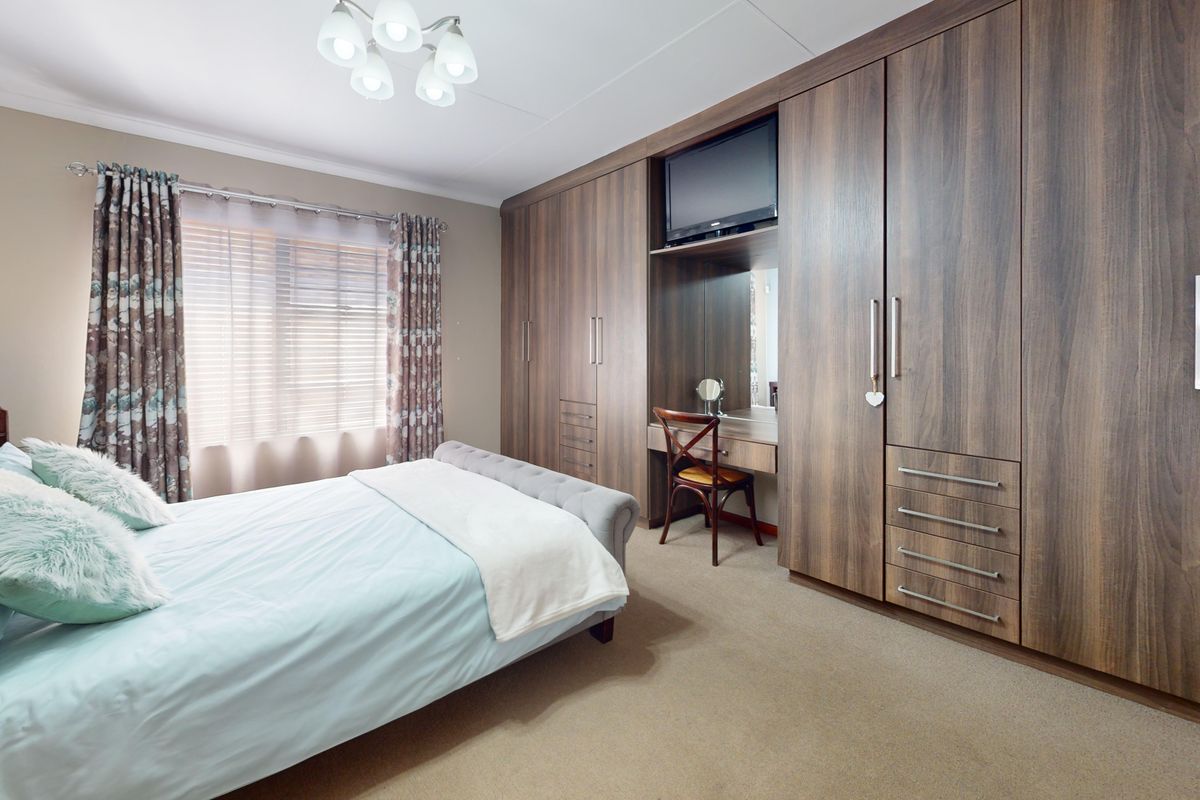 A well-maintained bedroom featuring extensive floor-to-ceiling built-in wooden cabinetry with an integrated vanity station and neutral carpeting.