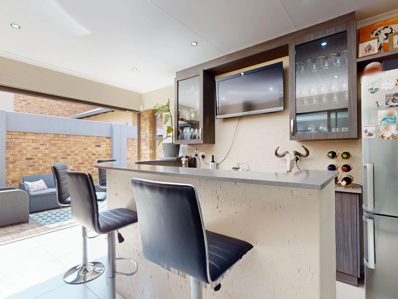 A well-appointed indoor bar area featuring built-in cabinetry, a stone-topped counter, and seamless access to an outdoor patio through bi-fold doors.