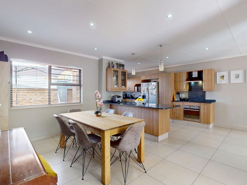 Spacious open-plan kitchen and dining area featuring modern wood-finish cabinetry, a central island, integrated appliances, and neutral tiled flooring throughout.