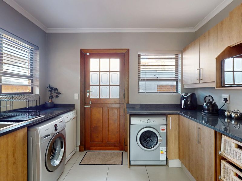 A functional laundry room featuring built-in wooden cabinetry, dark laminate countertops, a stainless steel sink, and tiled flooring with direct exterior access.