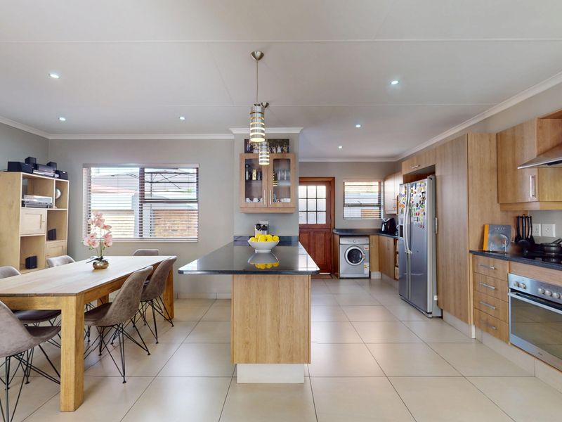Spacious open-plan kitchen and dining area featuring modern wooden cabinetry, granite countertops, a central island, and tiled flooring throughout.