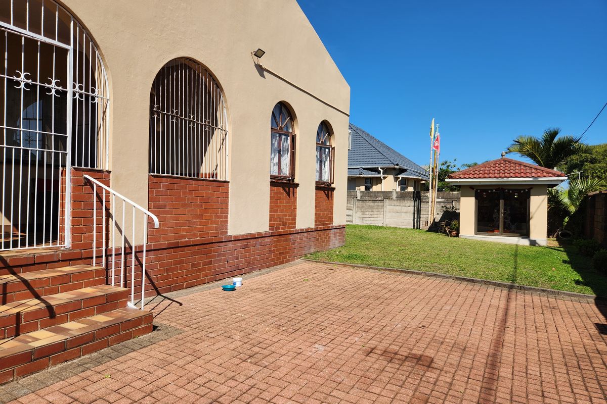 Rear exterior view of the house featuring brick paving, arched windows with security bars, and a separate outbuilding in the garden.