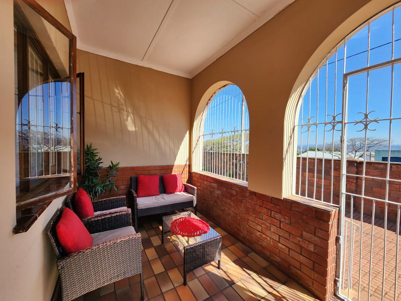 A covered patio area featuring brick wall accents, tiled flooring, and arched openings with security bars, offering an outdoor space for relaxation.