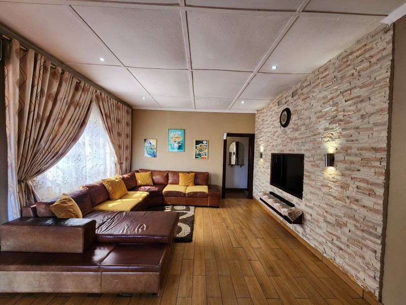 Spacious living room featuring a textured stone veneer feature wall, wood-look tiled flooring, and recessed ceiling lighting.