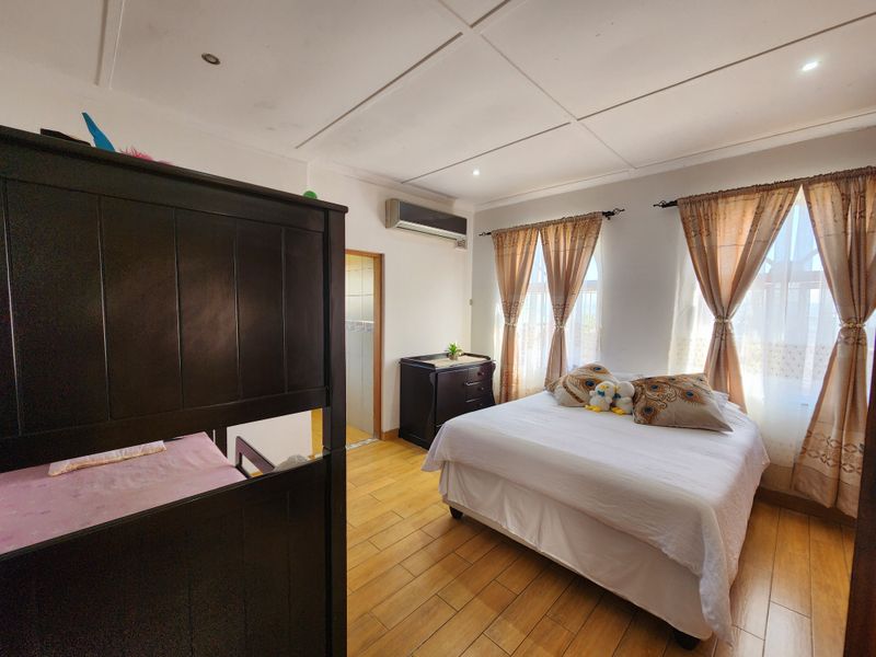 A spacious bedroom featuring tiled flooring, an integrated air conditioning unit, and direct access to an en-suite bathroom.