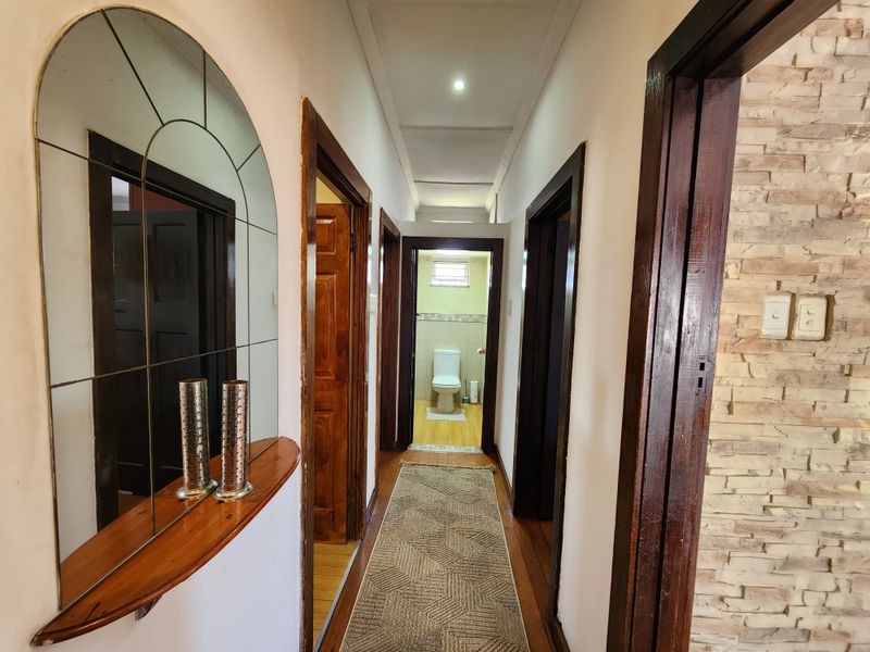 A well-lit hallway featuring wooden door frames, stone veneer wall accents, and wooden flooring, leading towards a bathroom at the end.