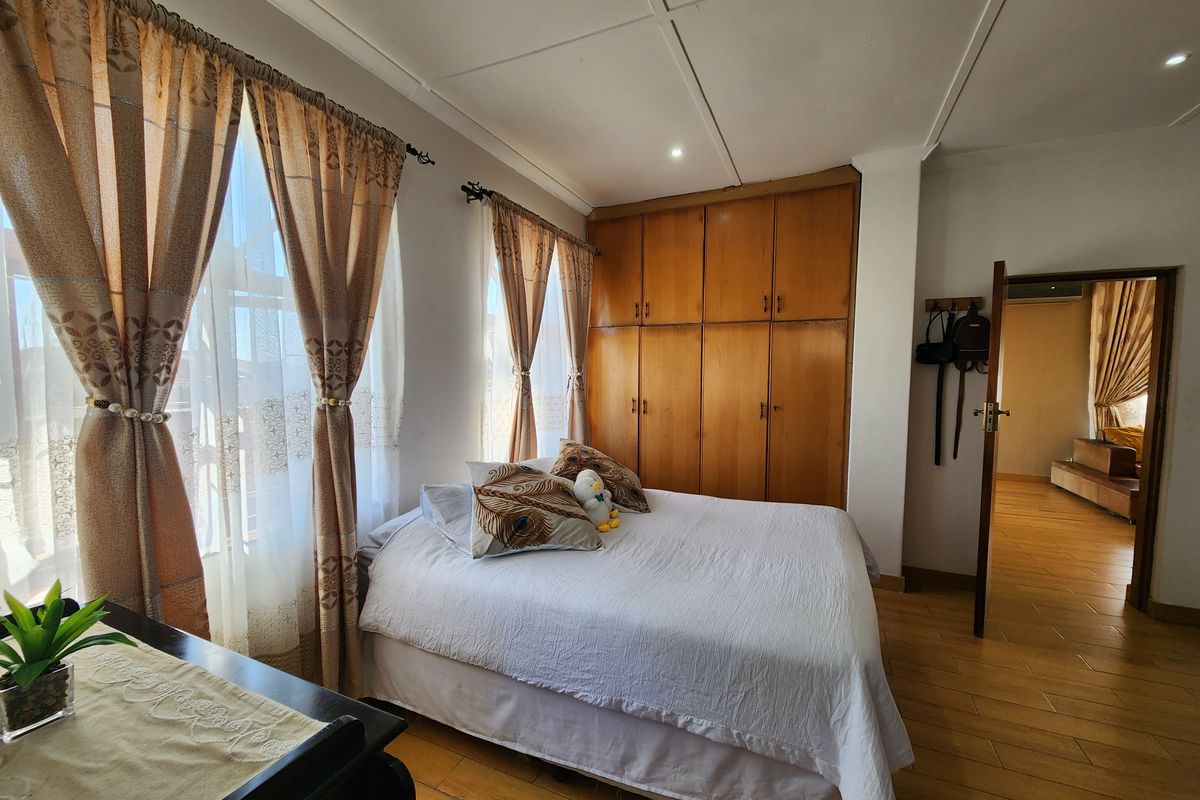 A bedroom featuring tiled flooring, built-in wooden cupboards, and natural light through large windows.