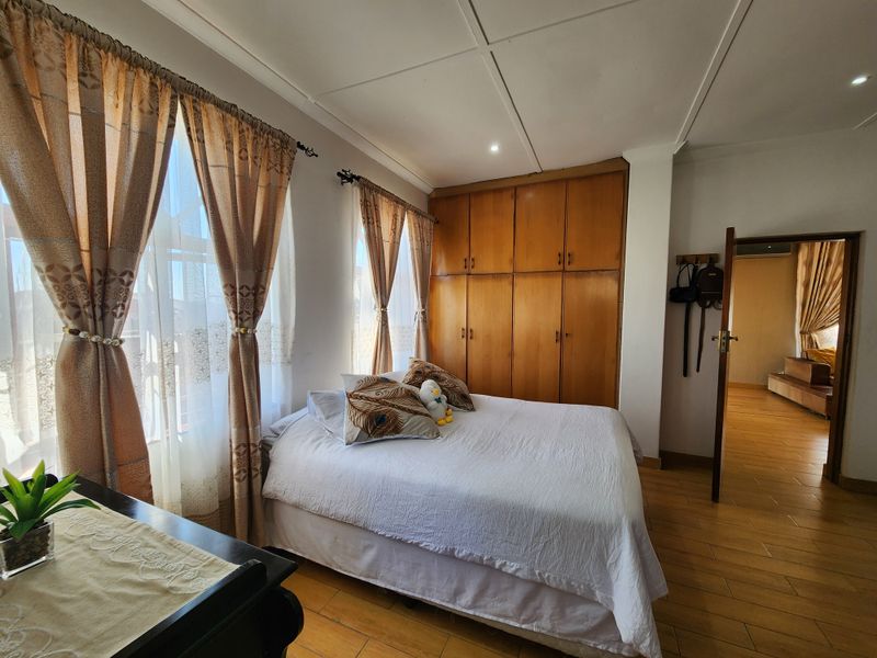 A bedroom featuring tiled flooring, built-in wooden cupboards, and natural light through large windows.