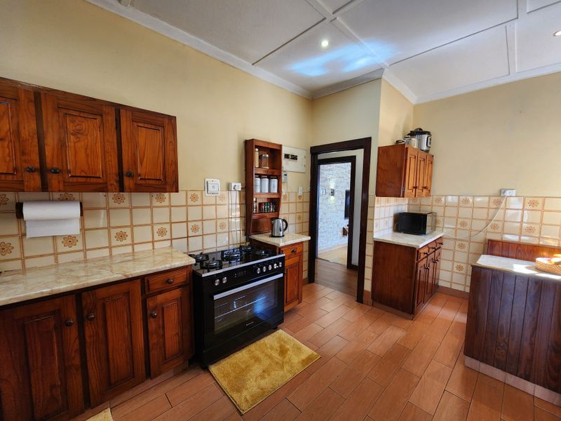 A functional kitchen featuring wooden cabinetry, stone-look countertops, a built-in gas stove and oven, and tiled flooring with classic wall tiling.