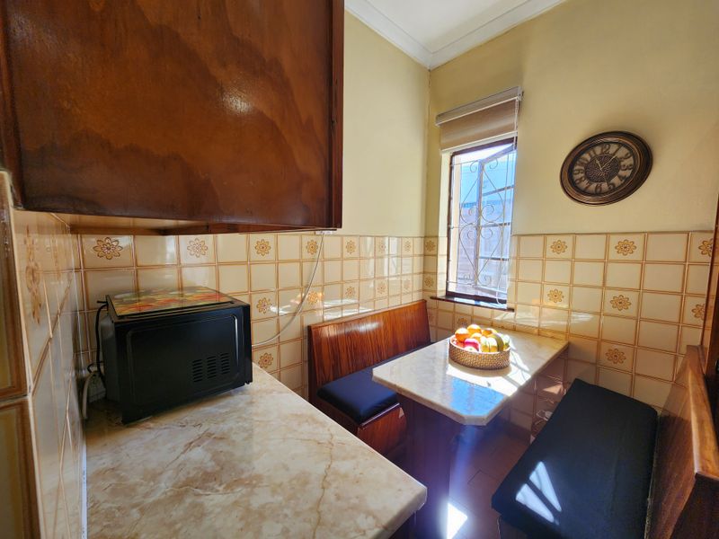 A compact kitchen area featuring dated wall tiles, stone-look countertops, and built-in wooden cabinetry with an integrated dining nook.