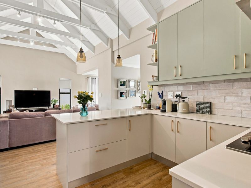 Modern open-plan kitchen featuring vaulted ceilings with exposed rafters, sleek cabinetry, quartz countertops, and a subway tile backsplash, flowing into the living area.