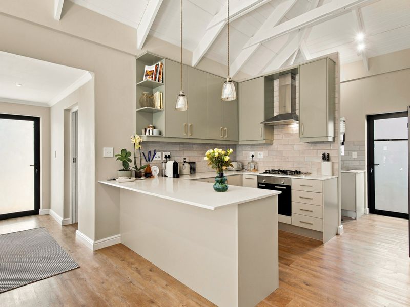 Modern kitchen featuring sage green cabinetry, stone countertops, gas hob, built-in oven, and vaulted ceilings with exposed rafters, creating a bright and airy space.