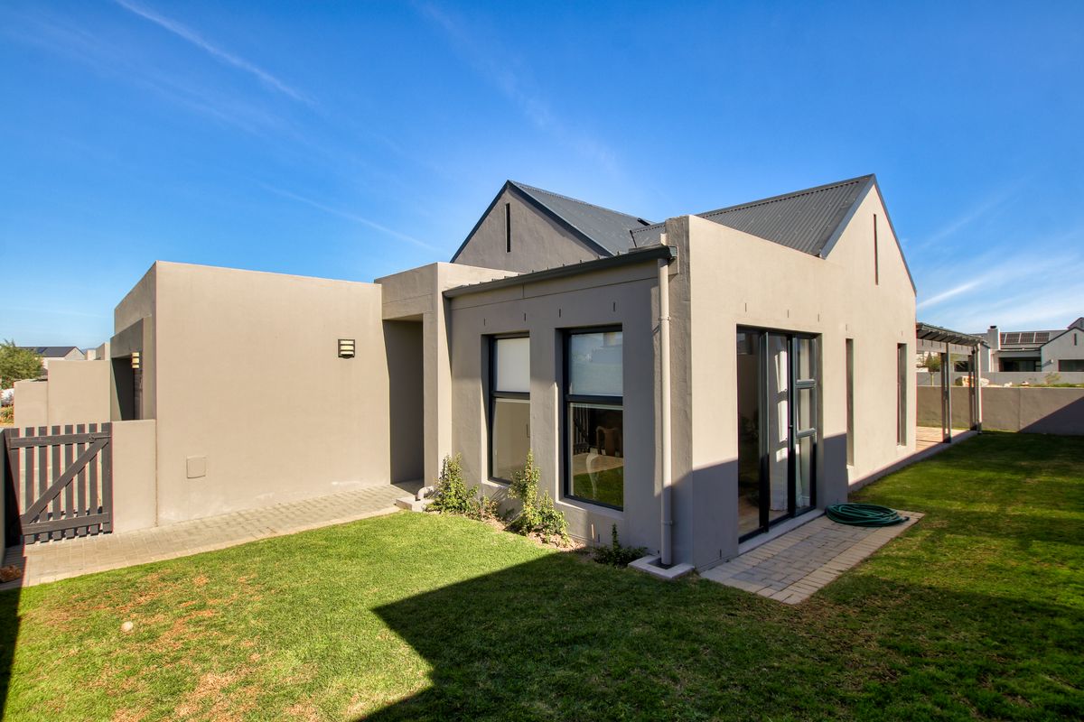 Rear view of a modern house featuring a metal roof, paved walkway, and sliding glass doors leading to a well-maintained garden area.