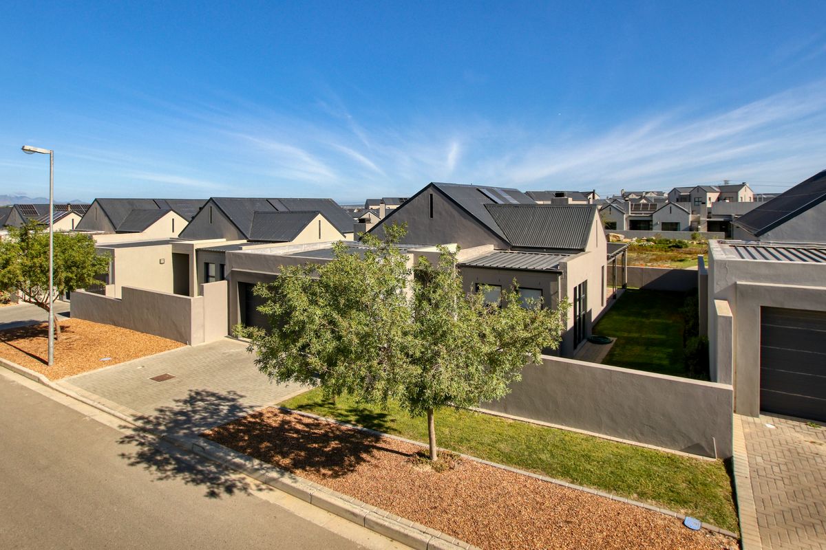 An elevated aerial view of a modern residential property featuring a paved driveway, metal roofing, and integrated solar panels within a suburban estate.