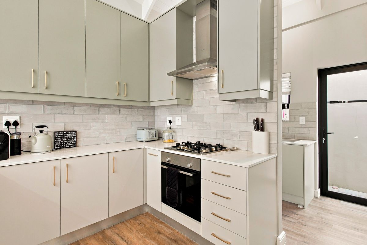Modern kitchen featuring sage green cabinetry, stone countertops, subway tile backsplash, and integrated stainless steel appliances, with an adjacent scullery area.