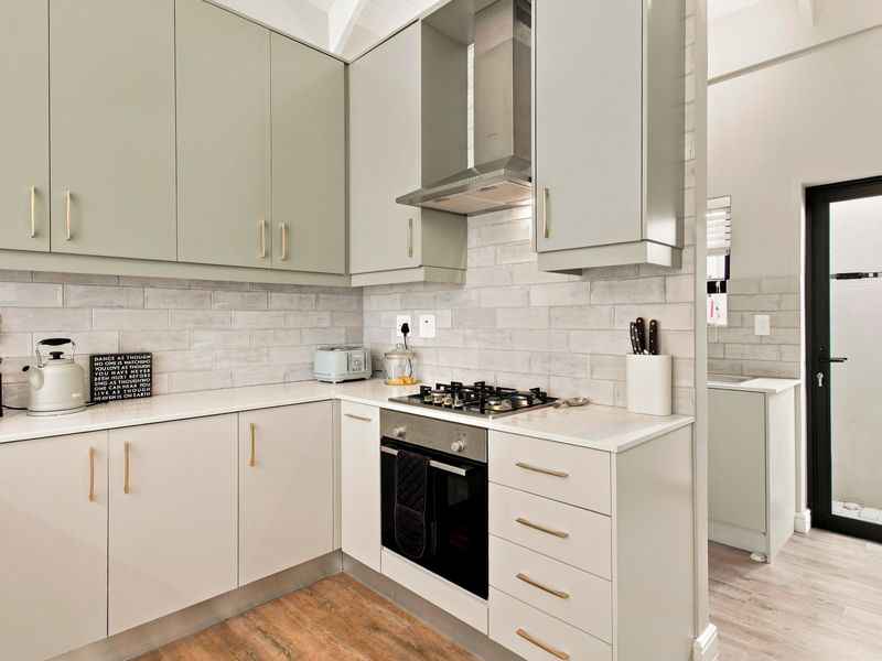 Modern kitchen featuring sage green cabinetry, stone countertops, subway tile backsplash, and integrated stainless steel appliances, with an adjacent scullery area.