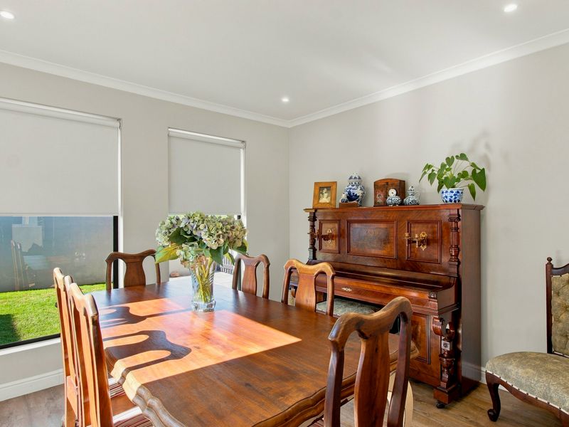 A bright and well-maintained dining room featuring timber-look flooring, recessed downlights, and roller blinds, offering a clean and neutral living space.