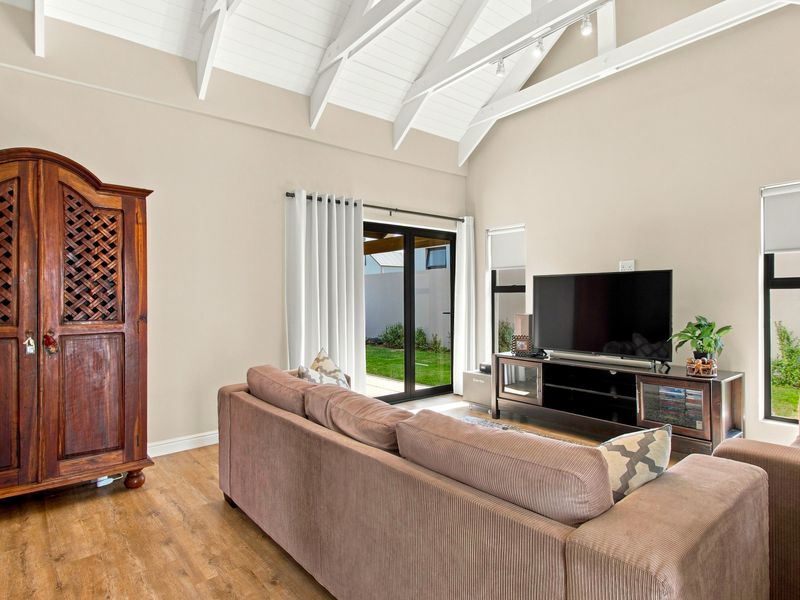 Spacious living room featuring high vaulted ceilings with exposed white timber trusses, laminate flooring, and direct access to the rear garden via sliding doors.
