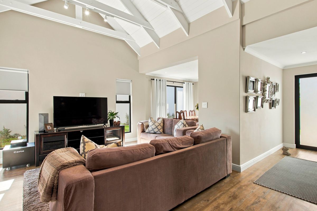 Spacious living room featuring a high vaulted ceiling with exposed rafters, track lighting, and durable laminate flooring, creating an open and airy atmosphere.