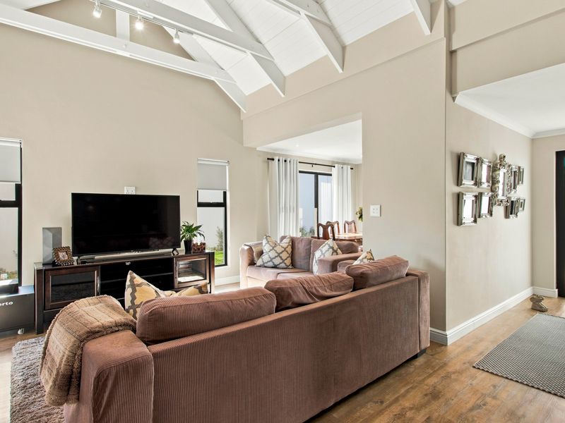 Spacious living room featuring a high vaulted ceiling with exposed rafters, track lighting, and durable laminate flooring, creating an open and airy atmosphere.