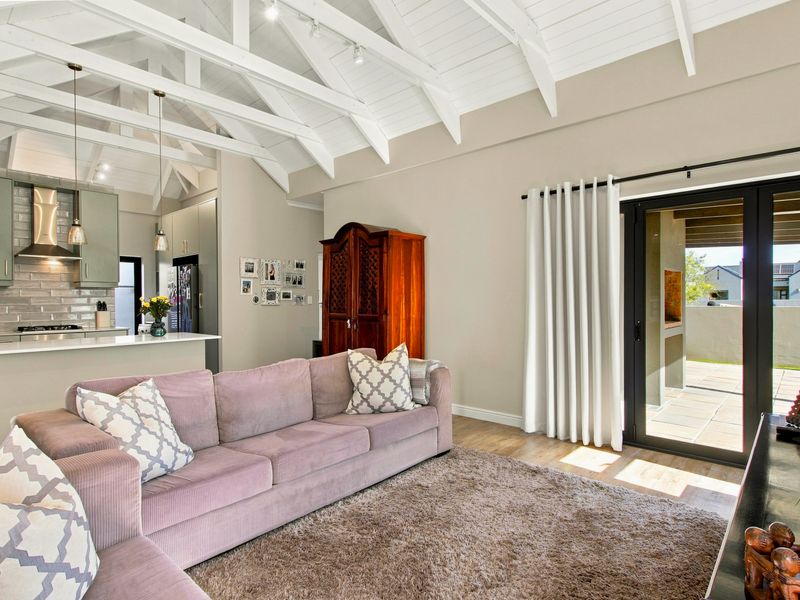 Spacious open-plan living area featuring a vaulted ceiling with exposed rafters, modern kitchen with stone countertops, and seamless access to an outdoor patio.