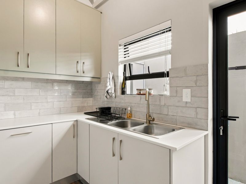 A clean and functional scullery featuring modern white cabinetry, subway tile backsplash, double stainless steel sink, and direct access to an outdoor area.