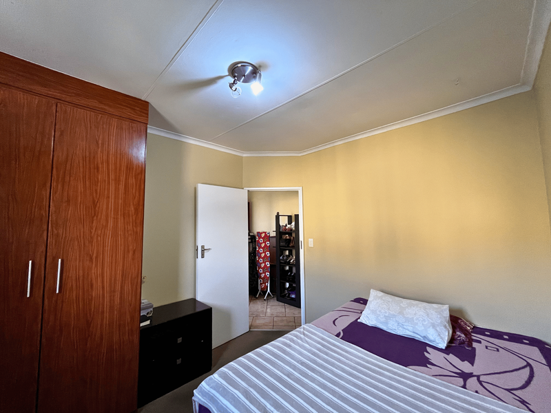 A standard bedroom featuring a built-in wooden wardrobe, coved ceiling, and neutral wall finishes, providing a functional sleeping space.