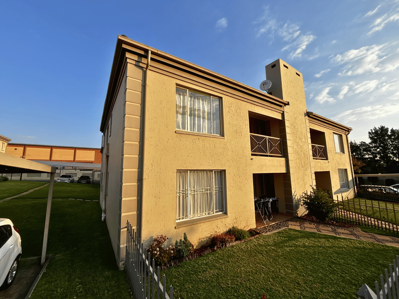 A two-story townhouse exterior featuring a textured stucco facade, balconies, and a chimney, set within a well-maintained residential complex with lawn and paved paths.