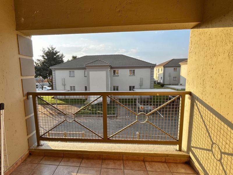 A covered balcony featuring tiled flooring and a decorative metal balustrade, offering an elevated view of the complex grounds and parking area.