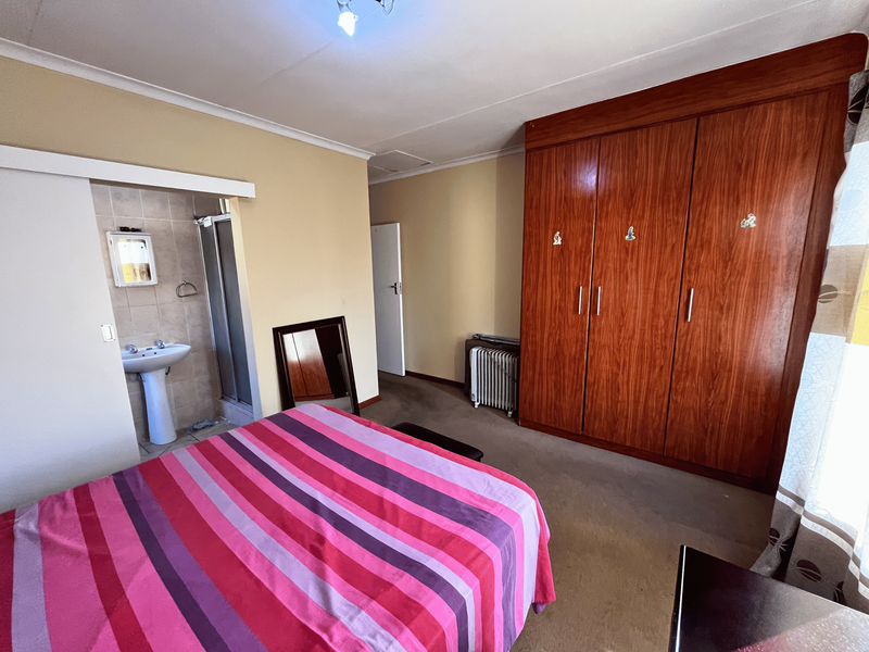 Bedroom featuring built-in wooden wardrobes and an en-suite bathroom with a pedestal basin and shower enclosure.