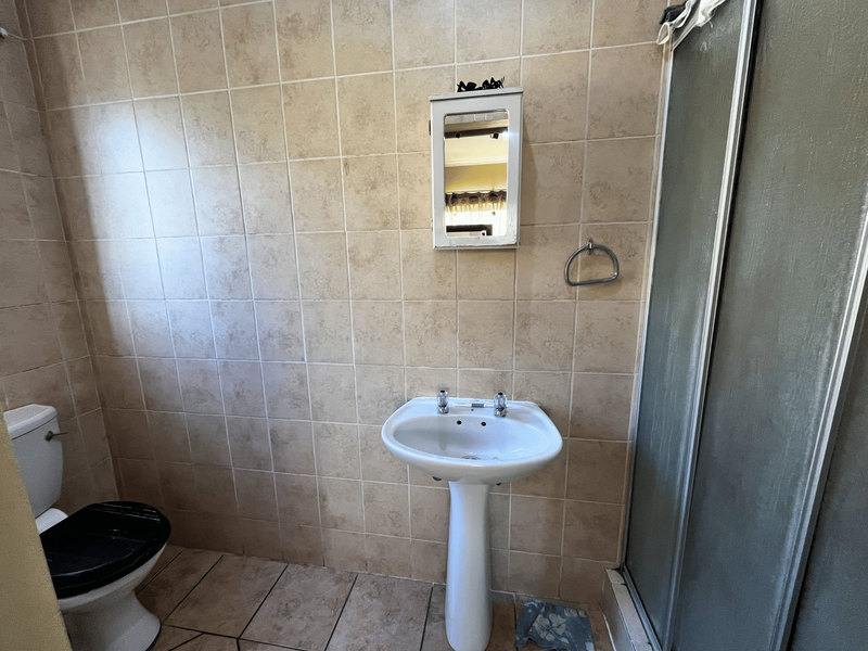 A dated bathroom featuring a pedestal basin, toilet, and shower enclosure with full-height wall tiling and floor tiles.