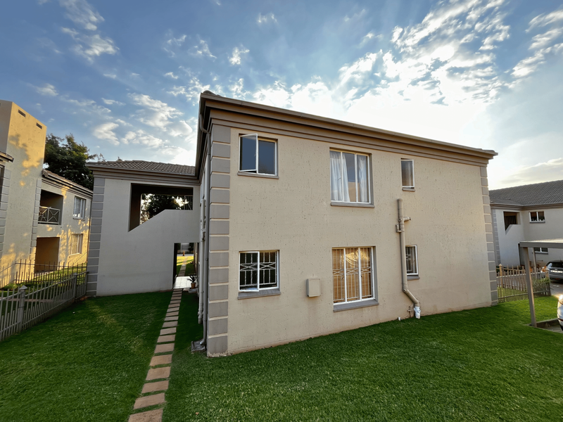 Rear view of a townhouse featuring a plastered facade, tiled roof, security bars on windows, and a well-maintained lawn with a paved walkway.