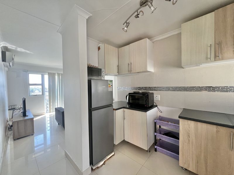 Open-plan kitchen and living area featuring light wood-finish cabinetry, dark countertops, tiled flooring, and an integrated air conditioning unit.
