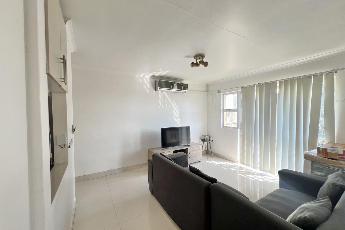 A bright living room featuring tiled flooring, an installed air conditioning unit, and vertical blinds allowing natural light into the space.