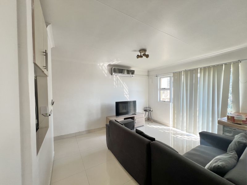 A bright living room featuring tiled flooring, an installed air conditioning unit, and vertical blinds allowing natural light into the space.