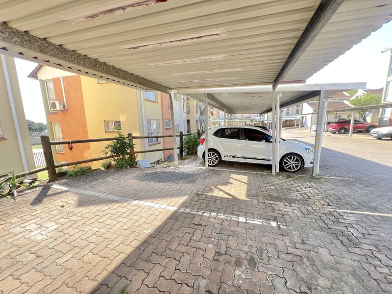 Covered carport parking area with paved surface and timber boundary railing located within an apartment complex.
