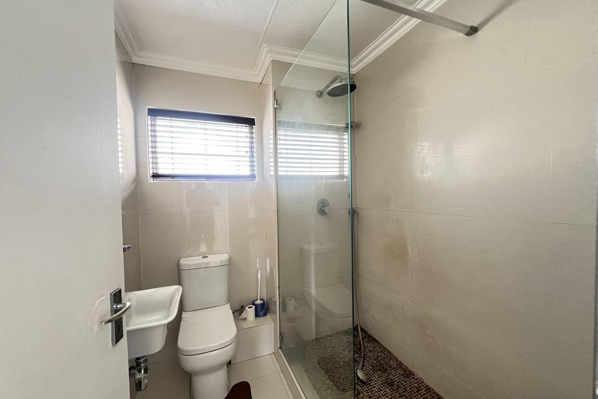 A functional bathroom featuring a glass-enclosed shower, wall-mounted basin, and toilet with neutral tiled finishes.