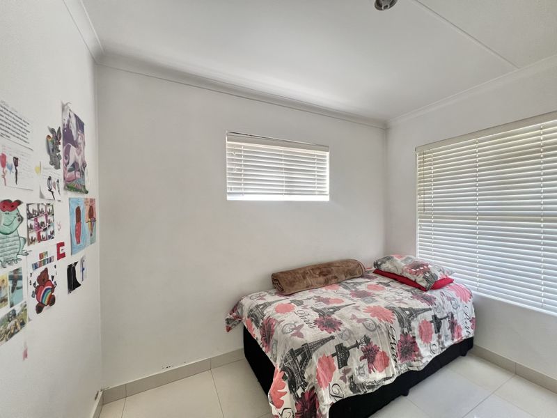 A functional bedroom featuring tiled flooring, coved ceilings, and dual windows fitted with venetian blinds.