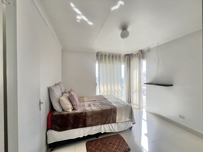 A bright bedroom featuring tiled flooring, neutral walls, and a sliding glass door providing access to an outdoor area.