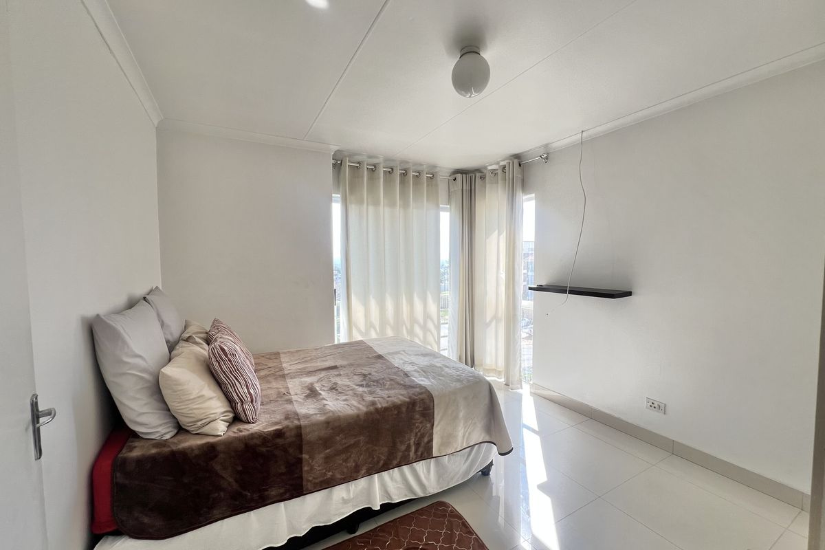 A bright bedroom featuring tiled flooring, a built-in wall shelf, and a sliding glass door providing natural light.
