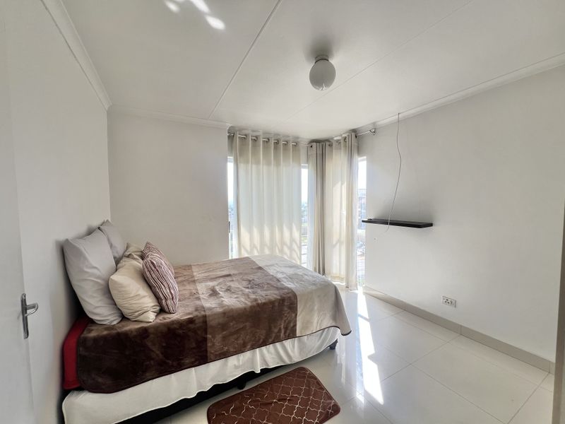 A bright bedroom featuring tiled flooring, a built-in wall shelf, and a sliding glass door providing natural light.