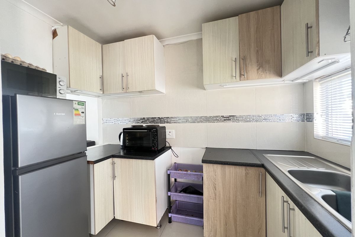 Compact kitchen featuring light wood-look laminate cabinetry, dark countertops, tiled backsplash, and a stainless steel sink.