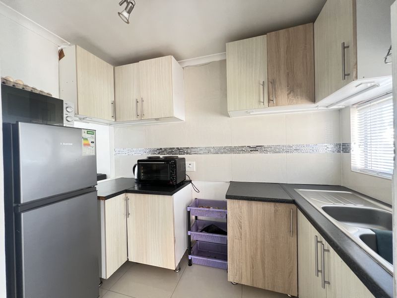 Compact kitchen featuring light wood-look laminate cabinetry, dark countertops, tiled backsplash, and a stainless steel sink.